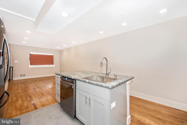 kitchen featuring light stone counters, dishwashing machine, an island with sink, light wood-type flooring, and sink