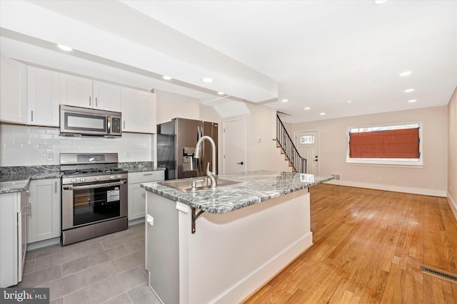 kitchen featuring stainless steel appliances, backsplash, an island with sink, sink, and light tile floors