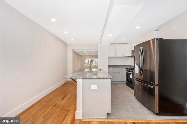 kitchen with stainless steel refrigerator with ice dispenser, light wood-type flooring, gas range oven, a kitchen bar, and white cabinetry