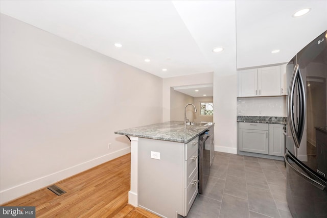 kitchen with tasteful backsplash, light tile floors, sink, a kitchen island with sink, and refrigerator