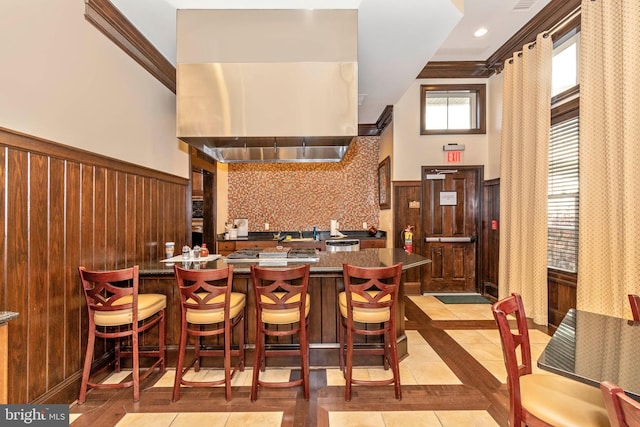 kitchen with light tile patterned flooring, a breakfast bar area, kitchen peninsula, backsplash, and crown molding