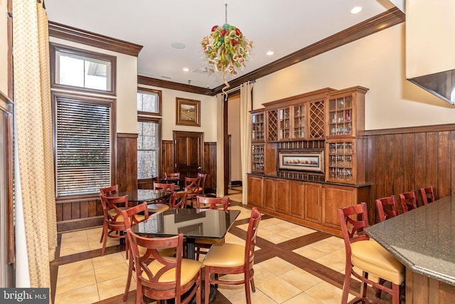 dining room with crown molding, wooden walls, and light tile patterned floors