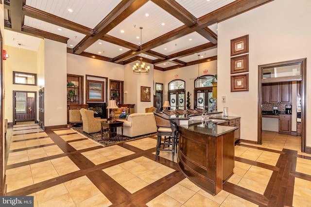 interior space featuring beamed ceiling, plenty of natural light, coffered ceiling, an inviting chandelier, and a high ceiling