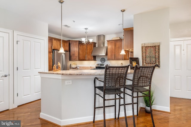 kitchen featuring appliances with stainless steel finishes, hanging light fixtures, wall chimney exhaust hood, and hardwood / wood-style floors