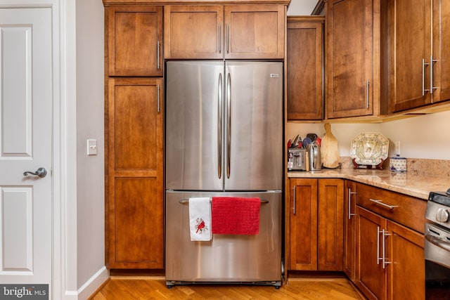 kitchen with light hardwood / wood-style flooring, appliances with stainless steel finishes, and light stone countertops