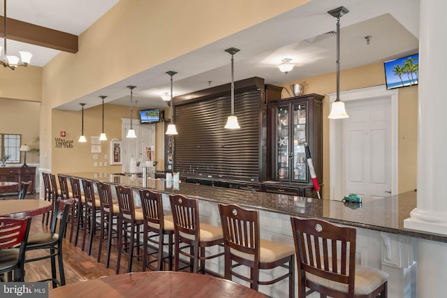 bar featuring dark stone counters, dark brown cabinetry, dark wood-type flooring, a chandelier, and hanging light fixtures