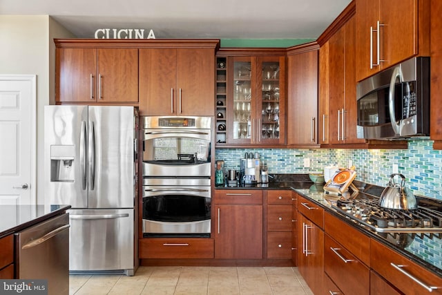 kitchen with backsplash, dark stone countertops, light tile patterned flooring, and stainless steel appliances