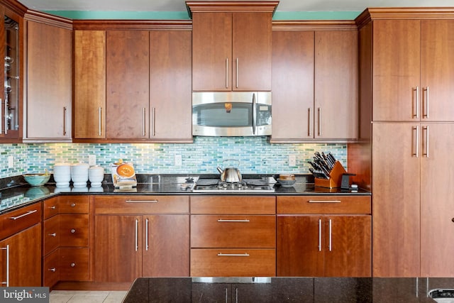 kitchen with light tile patterned flooring, backsplash, stainless steel appliances, and dark stone countertops