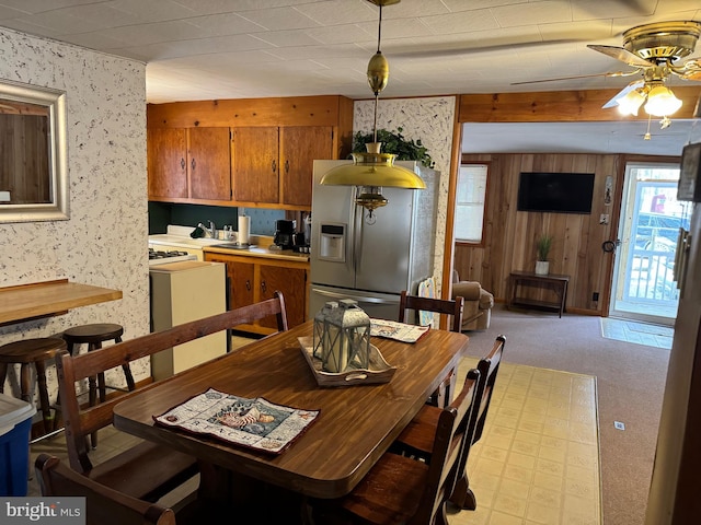 dining area featuring light colored carpet, wood walls, and ceiling fan