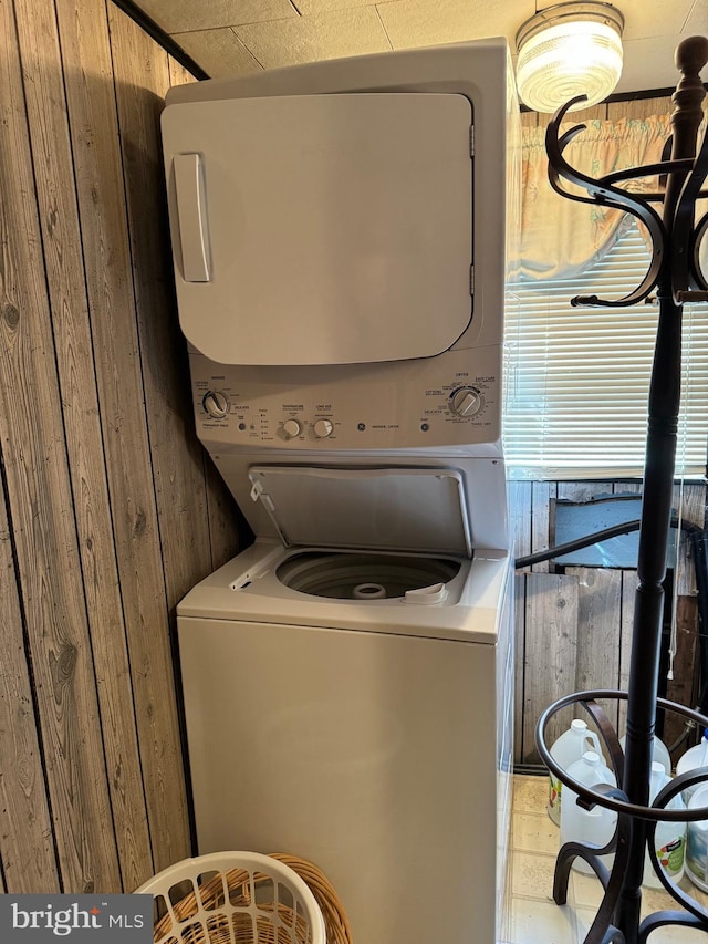 laundry area featuring wood walls, tile floors, and stacked washer and clothes dryer