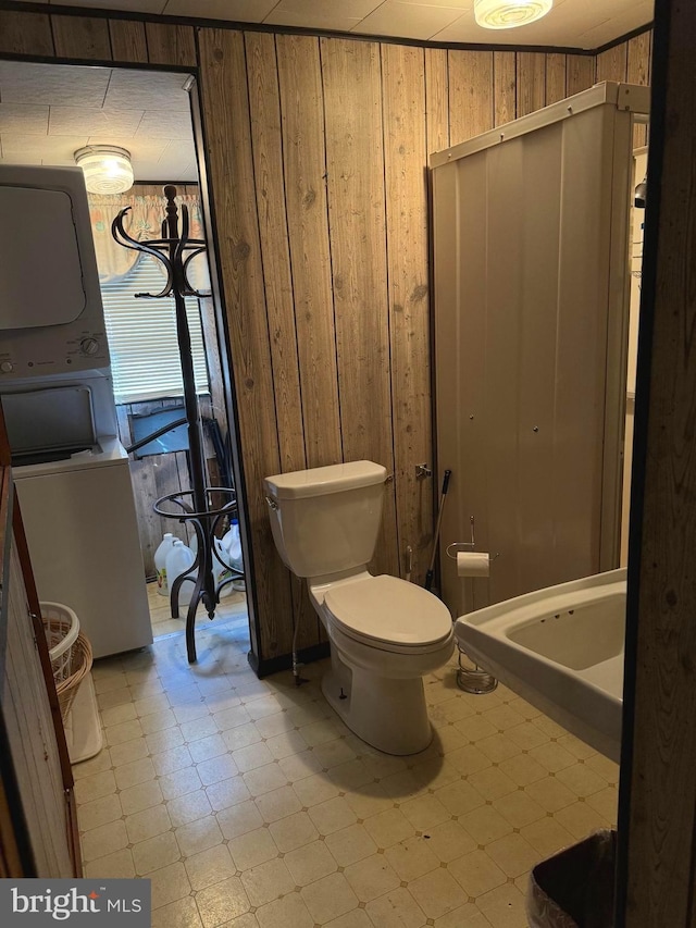 bathroom featuring tile flooring, stacked washer / dryer, toilet, and wooden walls