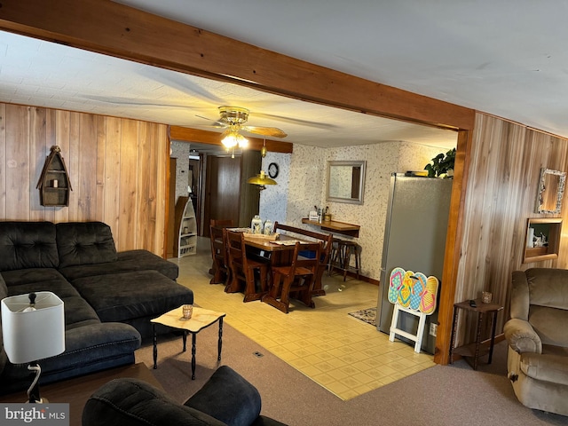 living room with ceiling fan, light tile flooring, wooden walls, and beam ceiling