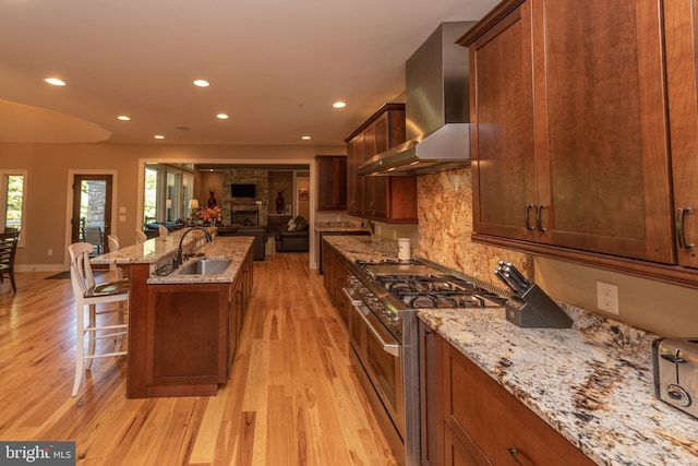 kitchen featuring wall chimney exhaust hood, range with two ovens, light hardwood / wood-style flooring, a kitchen bar, and sink