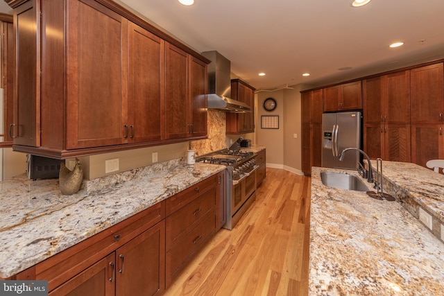 kitchen with light stone counters, appliances with stainless steel finishes, wall chimney range hood, and light hardwood / wood-style flooring