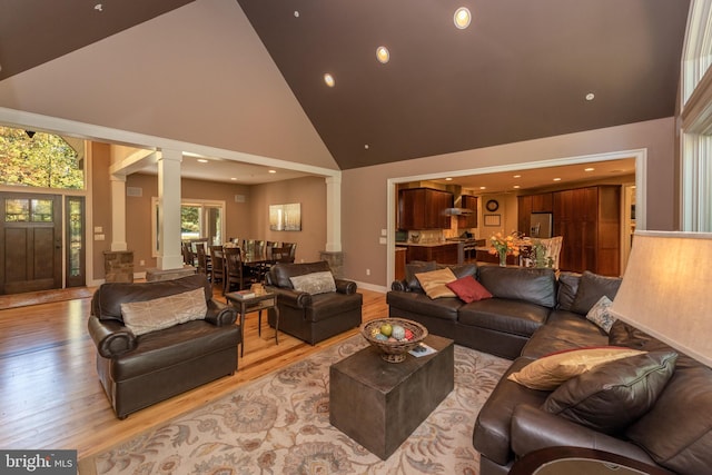 living room with light hardwood / wood-style flooring, high vaulted ceiling, and decorative columns