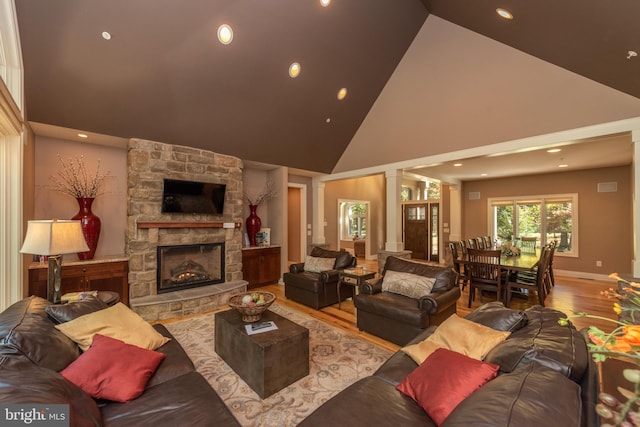 living room featuring high vaulted ceiling, light hardwood / wood-style flooring, decorative columns, and a fireplace