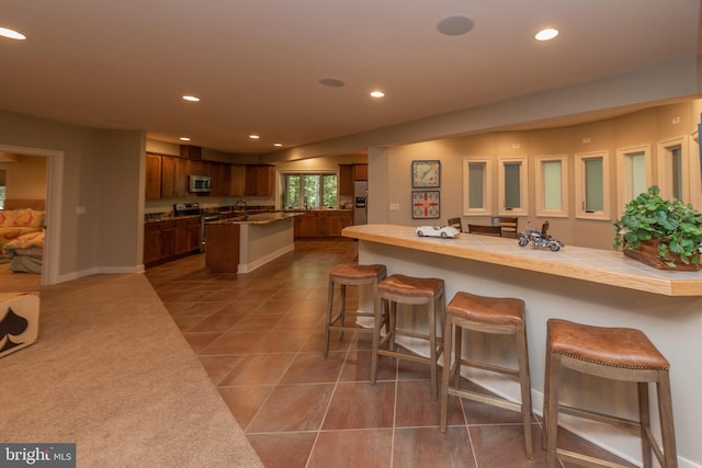 kitchen with appliances with stainless steel finishes, dark tile flooring, and a kitchen bar