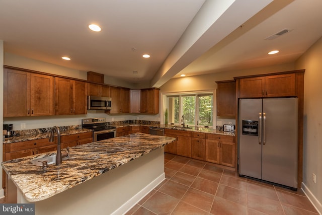 kitchen with appliances with stainless steel finishes, dark stone countertops, tile floors, and sink