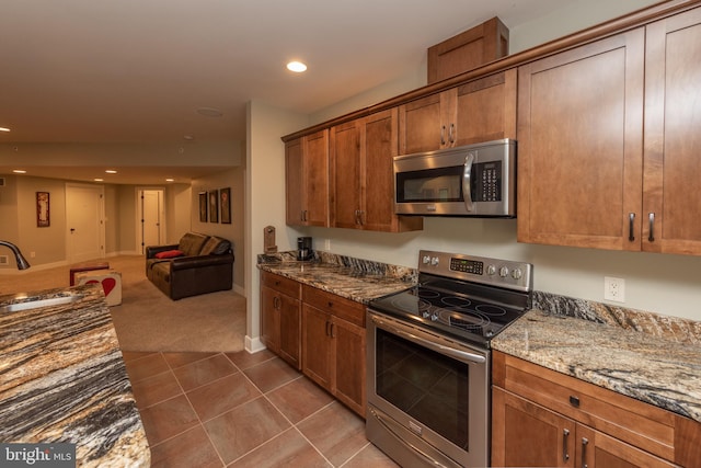 kitchen with light stone counters, appliances with stainless steel finishes, dark tile floors, and sink