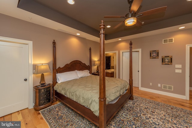 bedroom with a raised ceiling, ceiling fan, and light hardwood / wood-style floors