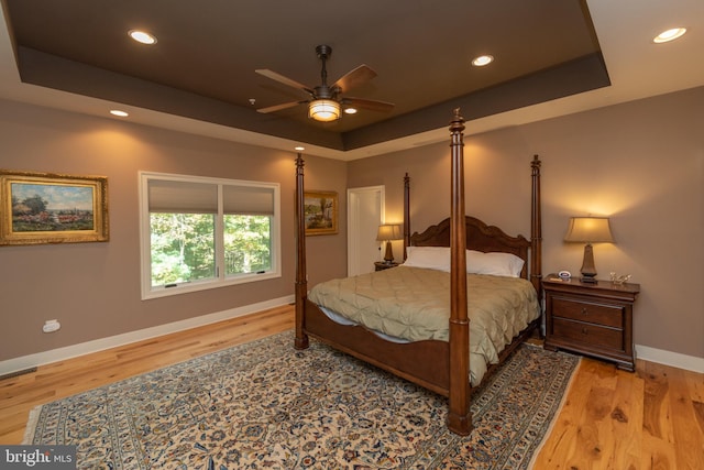 bedroom with a raised ceiling, ceiling fan, and light wood-type flooring