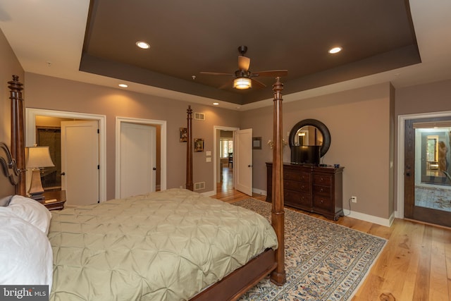 bedroom with ceiling fan, light hardwood / wood-style floors, a tray ceiling, and multiple windows