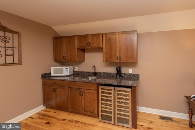 kitchen featuring light wood-type flooring, dark stone countertops, sink, and beverage cooler