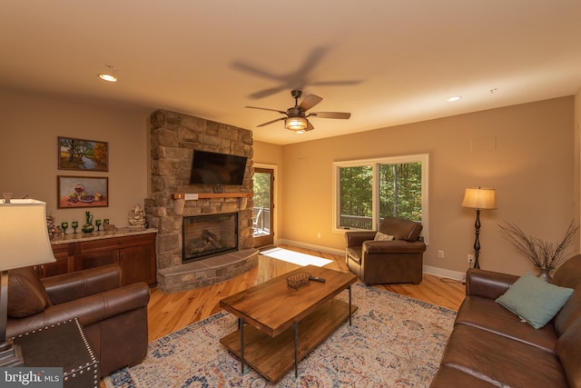 living room featuring a stone fireplace, light hardwood / wood-style floors, and ceiling fan