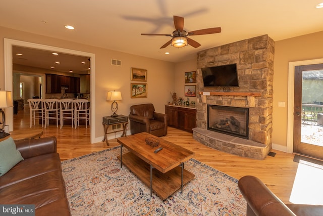 living room featuring light hardwood / wood-style flooring, ceiling fan, and a stone fireplace