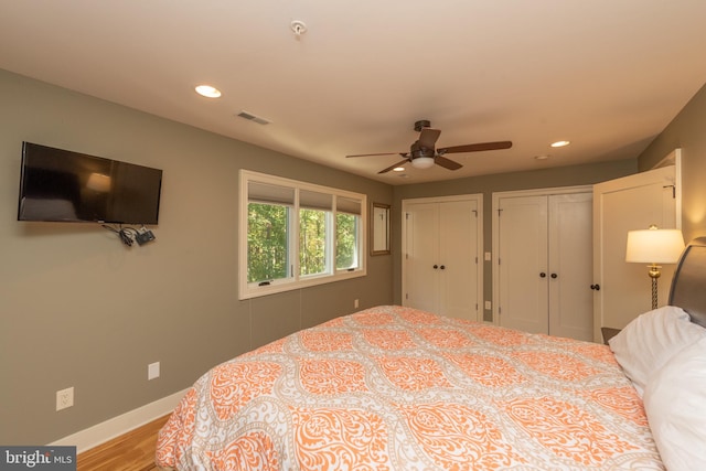 bedroom featuring light hardwood / wood-style floors, ceiling fan, and two closets