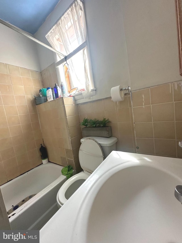 bathroom with tiled shower / bath, tile walls, and toilet