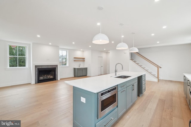 kitchen with light countertops, stainless steel microwave, a sink, and light wood-type flooring