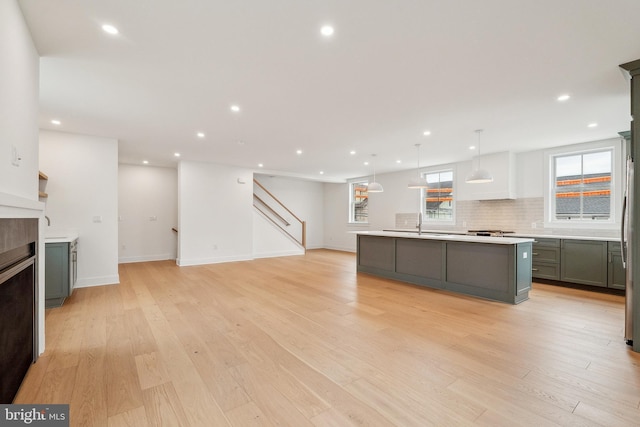 kitchen with decorative backsplash, a center island with sink, light countertops, gray cabinets, and a tiled fireplace