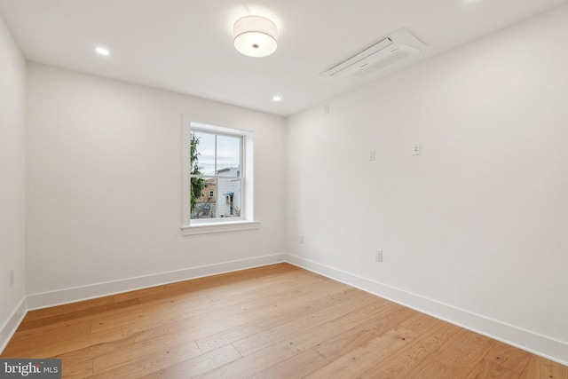 unfurnished room with baseboards, a wall unit AC, and light wood finished floors