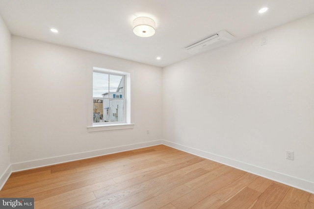 empty room with an AC wall unit, baseboards, and light wood finished floors