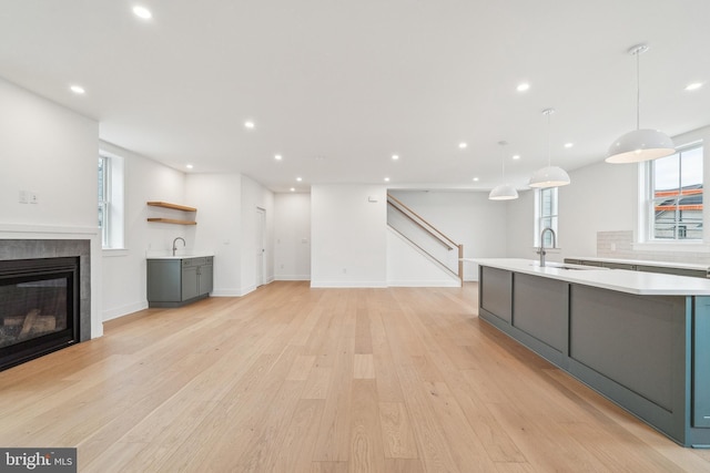 kitchen with light countertops, gray cabinetry, a sink, light wood-style flooring, and an island with sink