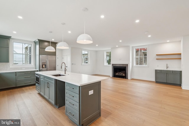 kitchen featuring a sink, light wood finished floors, stainless steel fridge with ice dispenser, light countertops, and a tiled fireplace