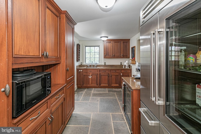 kitchen featuring built in appliances, light stone counters, sink, and dark tile floors