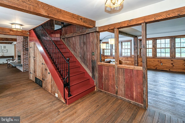 staircase featuring brick wall, beamed ceiling, and dark hardwood / wood-style floors