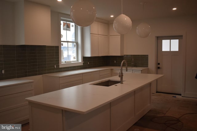 kitchen featuring white cabinetry, a center island with sink, hanging light fixtures, and sink