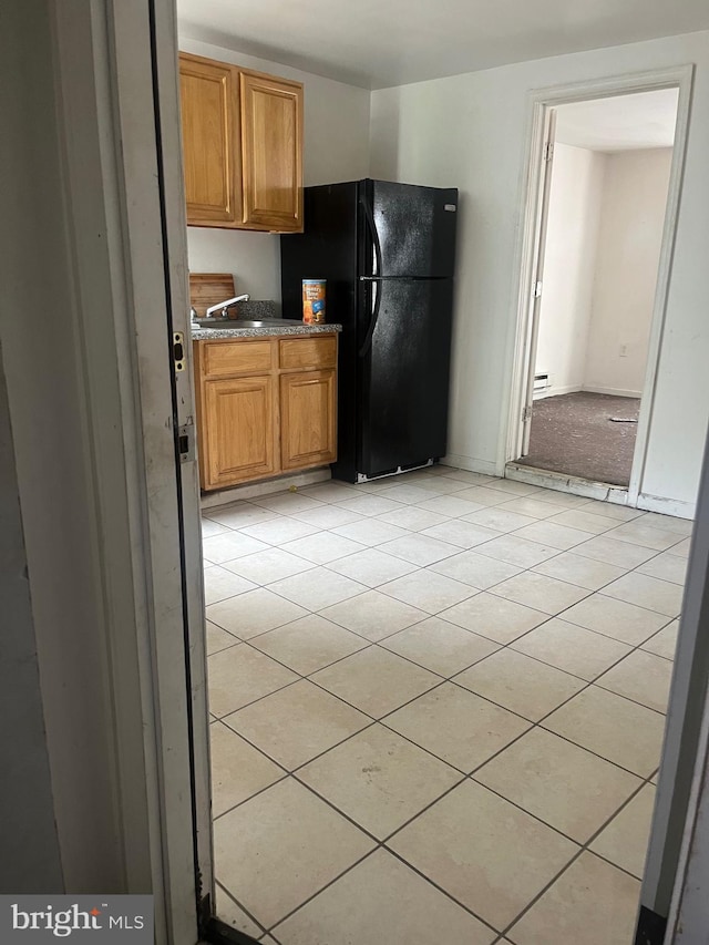 kitchen featuring sink, light tile floors, and black fridge