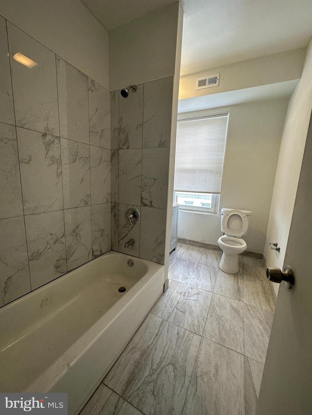 bathroom with tiled shower / bath combo, toilet, and tile flooring