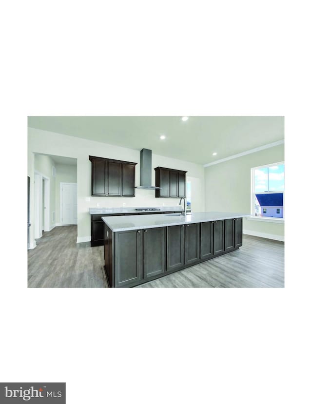 kitchen featuring sink, hardwood / wood-style floors, wall chimney range hood, and a kitchen island with sink