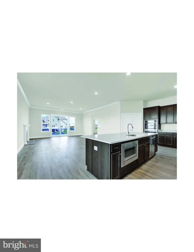 kitchen with appliances with stainless steel finishes, light hardwood / wood-style floors, dark brown cabinets, and a center island with sink