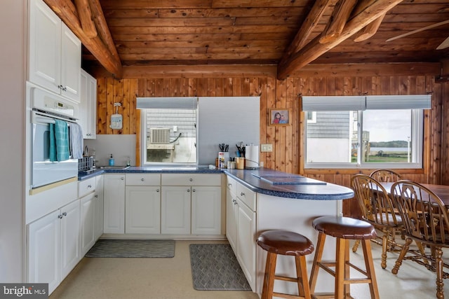 kitchen with wood ceiling, kitchen peninsula, oven, and white cabinets