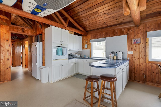 kitchen with a kitchen breakfast bar, white appliances, white cabinetry, wooden ceiling, and vaulted ceiling with beams