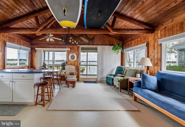 carpeted living room with wooden ceiling, ceiling fan, wood walls, and lofted ceiling with beams