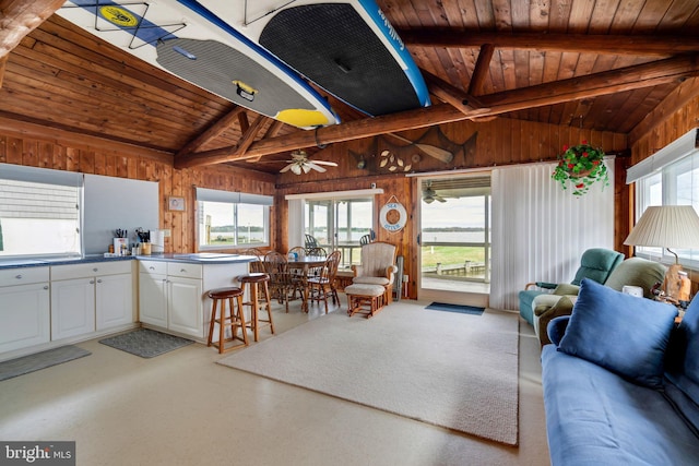 kitchen featuring wooden walls, white cabinetry, vaulted ceiling with beams, wooden ceiling, and ceiling fan