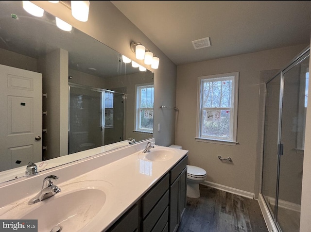 bathroom featuring double sink, an enclosed shower, wood-type flooring, vanity with extensive cabinet space, and toilet