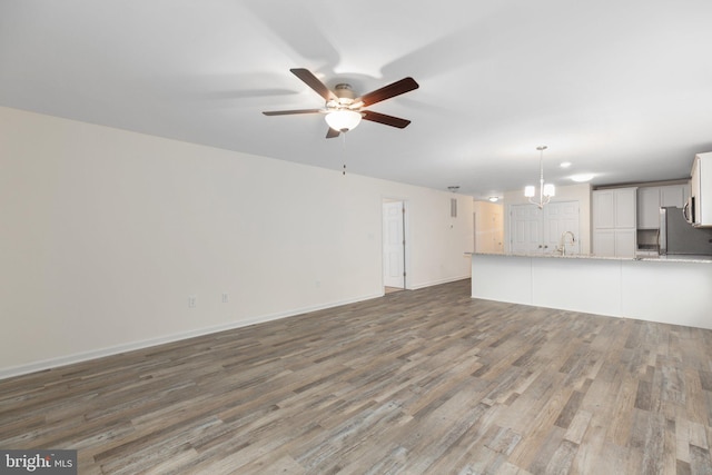 unfurnished living room featuring sink, ceiling fan with notable chandelier, and hardwood / wood-style flooring